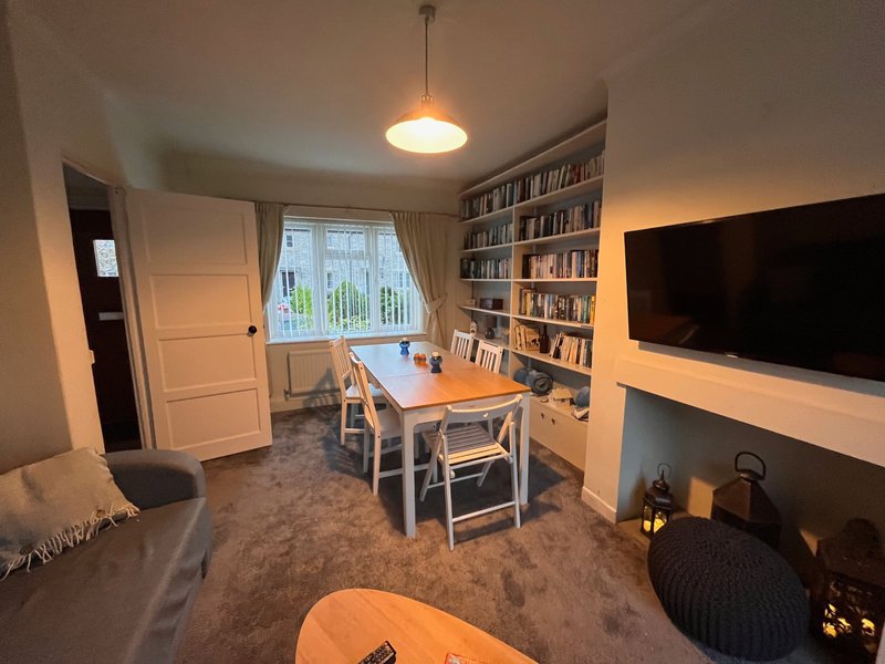Living room with bookshelves, wooden table, chairs, TV, and window with garden view