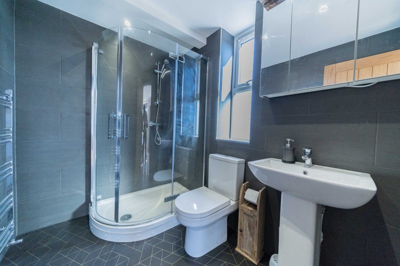 Modern bathroom with curved shower enclosure, toilet, white pedestal sink and dark tiling