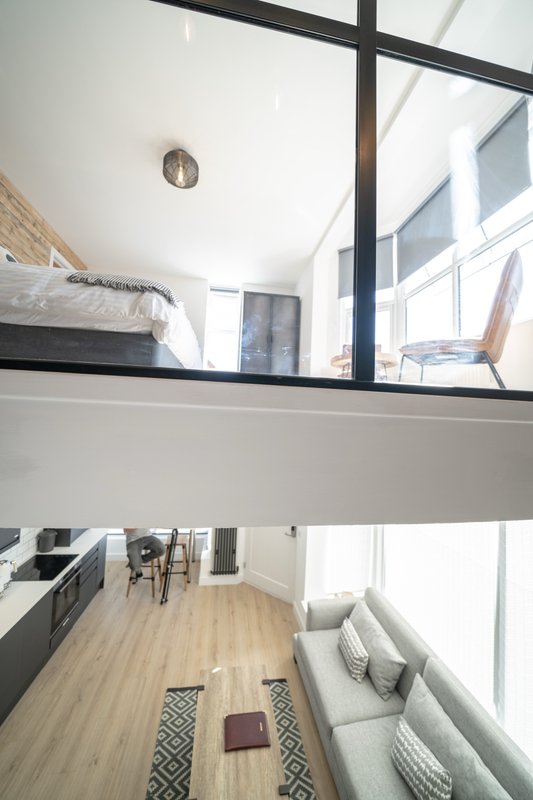 Modern loft-style studio with mezzanine bedroom, open kitchen, and bright windows