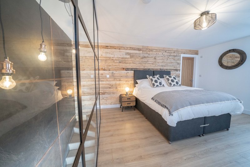 Modern bedroom with double bed, wooden accent wall, pendant lights and ensuite bathroom