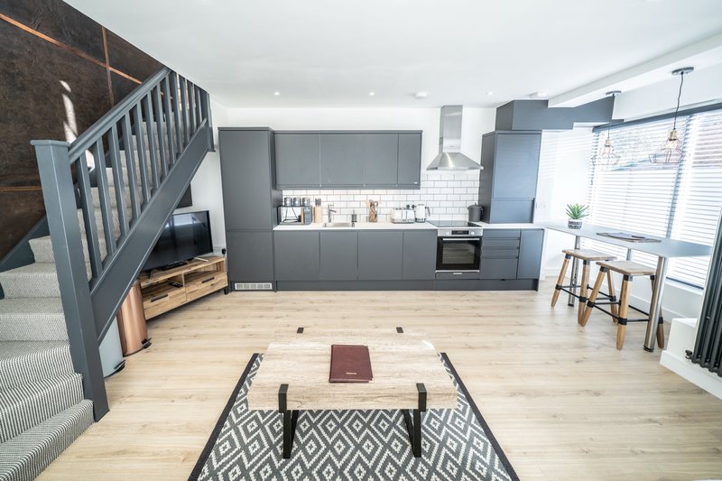 Open-plan kitchen and living area with grey cabinetry, wooden flooring, staircase and dining table