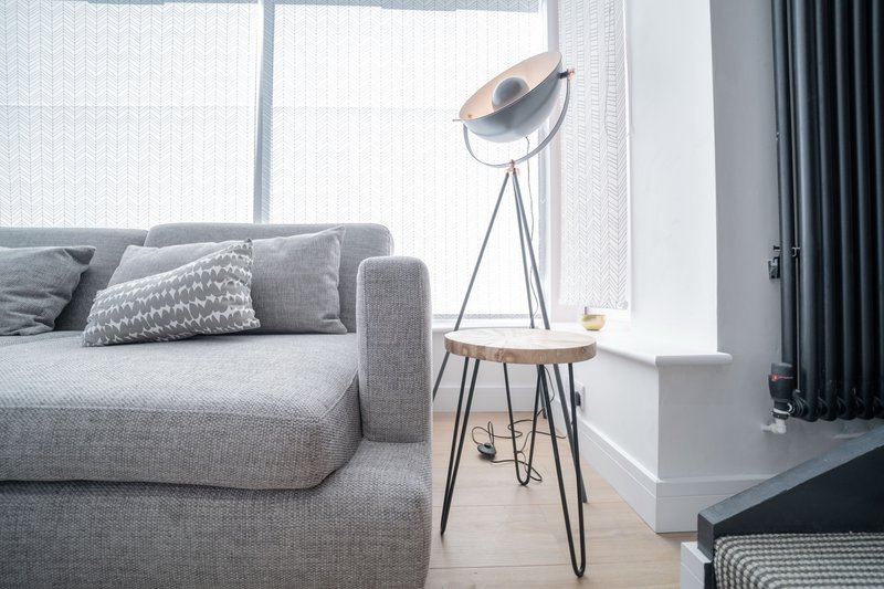 Modern living room with grey sofa, tripod floor lamp, small side table and large windows