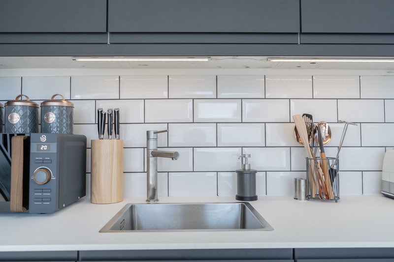 Modern kitchen sink with white subway tile backsplash, stainless steel faucet, and organized countertop storage