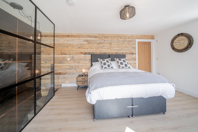 Modern bedroom with double bed, wooden feature wall, ensuite shower and wooden flooring