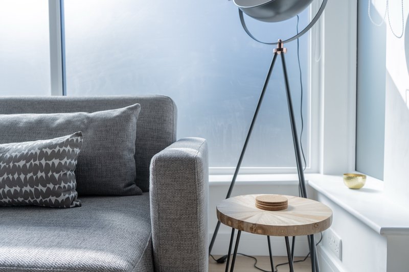 Modern living room with gray sofa, patterned cushions, wooden side table, and tripod floor lamp