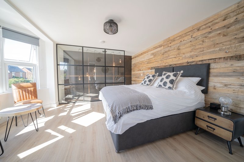 Modern bedroom with double bed, wooden accent wall, glass wardrobe and window seat