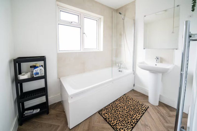 Modern bathroom with white bathtub, pedestal sink, shower enclosure and wooden flooring