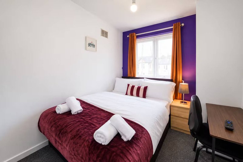 Modern bedroom with double bed, burgundy quilt, purple accent wall and gold curtains