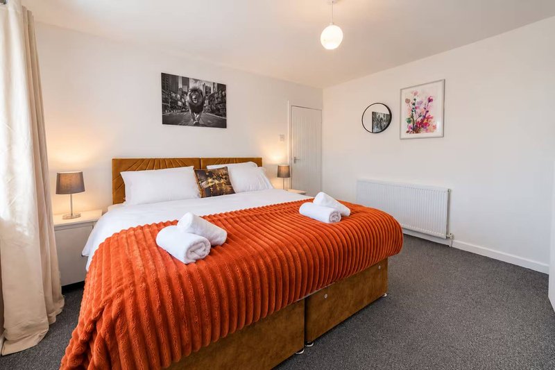 Bright bedroom with wooden bed frame, orange bedding, white pillows and wall art
