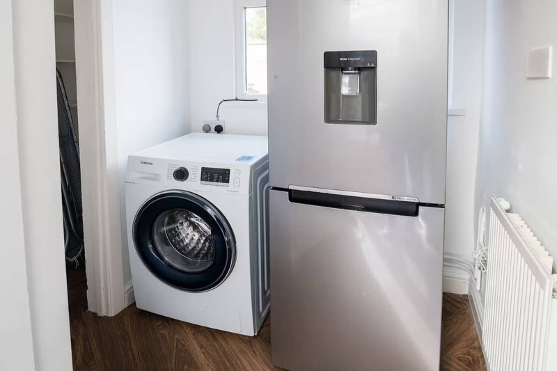 Utility room with white washing machine, stainless steel refrigerator, and wooden flooring