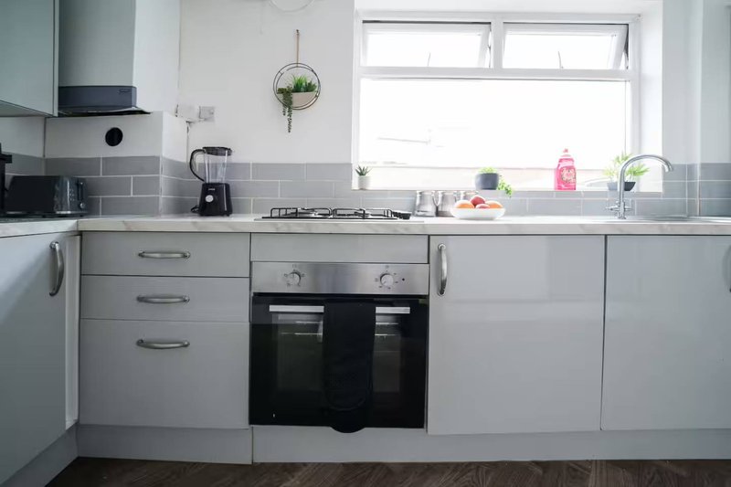 Modern white kitchen with gray subway tile backsplash, black oven, and window above sink