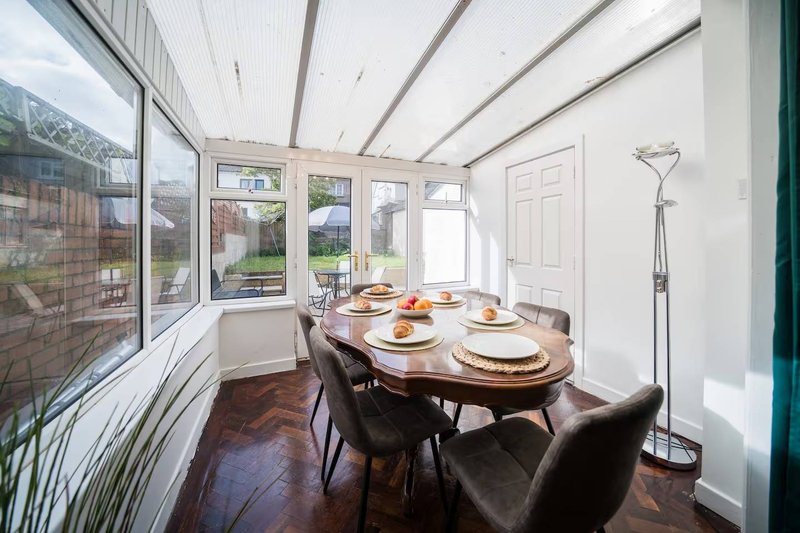 Bright conservatory dining room with oval table, place settings and garden views