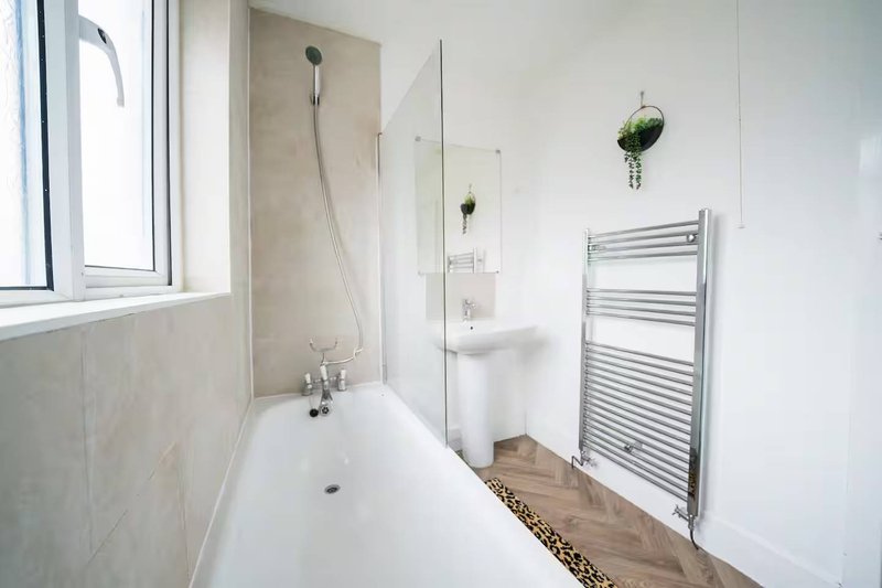 Modern bathroom with white bathtub, glass shower partition, heated towel rail and window