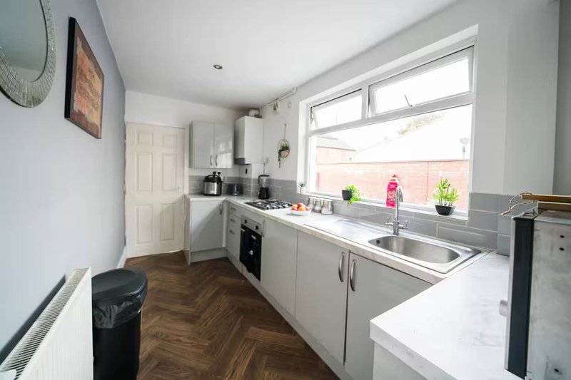 Modern kitchen with white cabinetry, stainless steel sink, window over countertop and wooden flooring