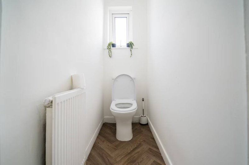 Clean white bathroom with toilet, radiator, small window and herringbone wood flooring