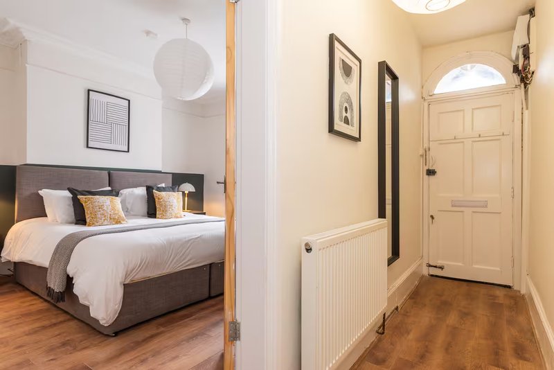 Modern bedroom with gray bed, white bedding, wooden floor, and hallway entrance visible