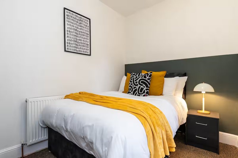 Modern bedroom with double bed, yellow throw, patterned cushions and bedside lamp