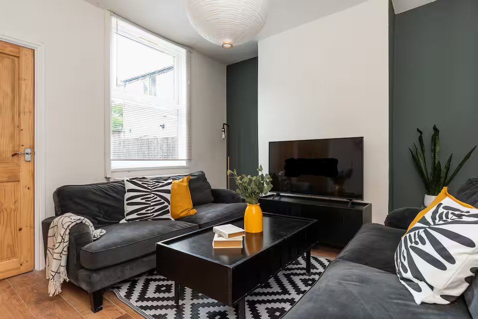 Modern living room with black sofa, TV, geometric patterned rug and accent cushions