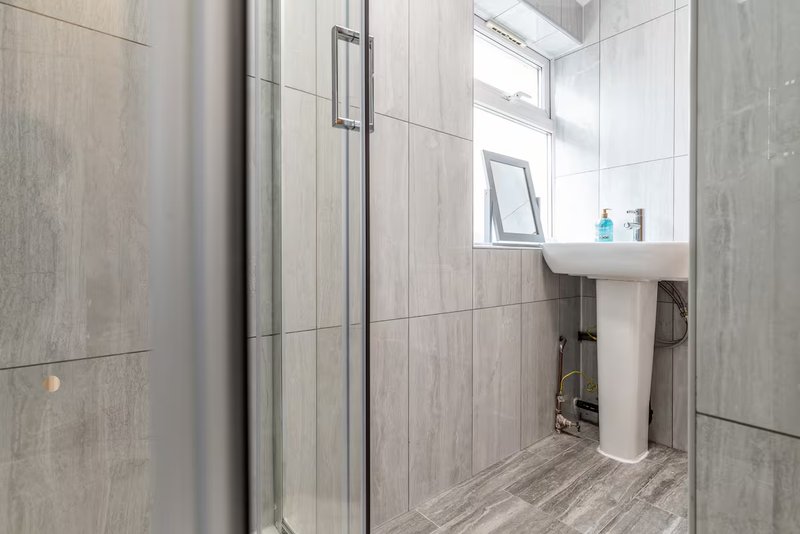 Modern bathroom with walk-in shower, pedestal sink, and tiled walls
