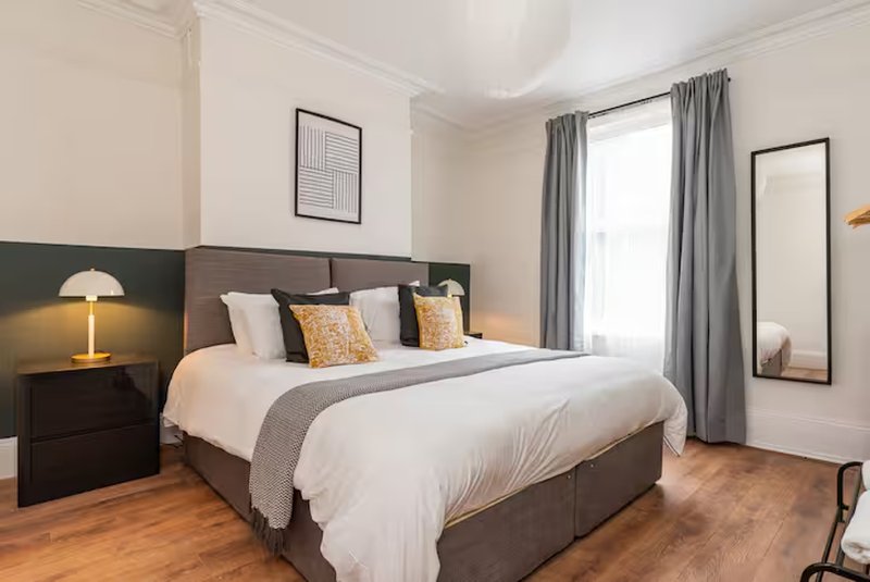 Modern bedroom with grey upholstered bed, white bedding, wooden floor and grey curtains