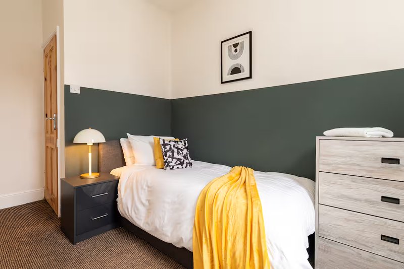 Bedroom with single bed, two-tone green and white walls, bedside lamp and wooden dresser