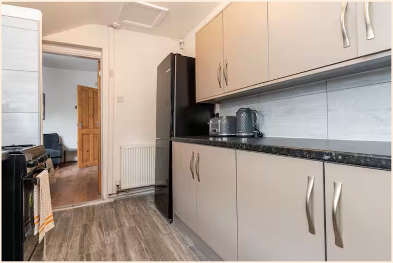Modern kitchen with cream cabinets, black worktop, black fridge and wooden flooring
