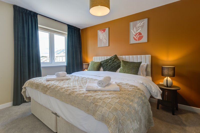 Bright bedroom with double bed, green cushions, orange walls, window with blue curtains