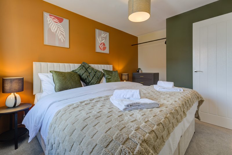 Bedroom with double bed, white headboard, green cushions, orange accent wall and pendant light