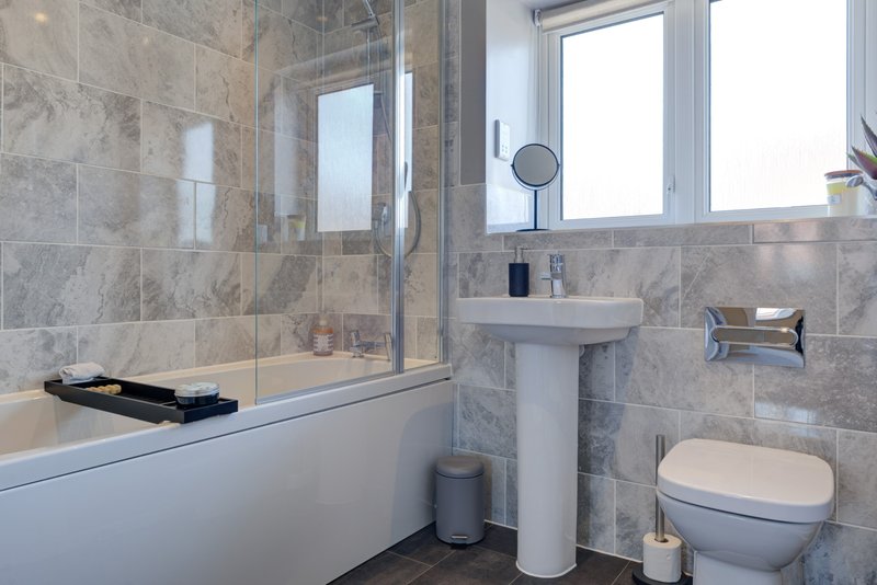Modern bathroom with grey tile walls, pedestal sink, toilet, and shower enclosure