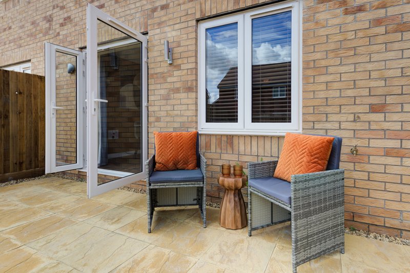 Brick patio with seating area, rattan chairs with orange cushions and glass doors