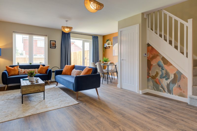 Open-plan living room with navy sofa, orange accents, wooden floor and staircase