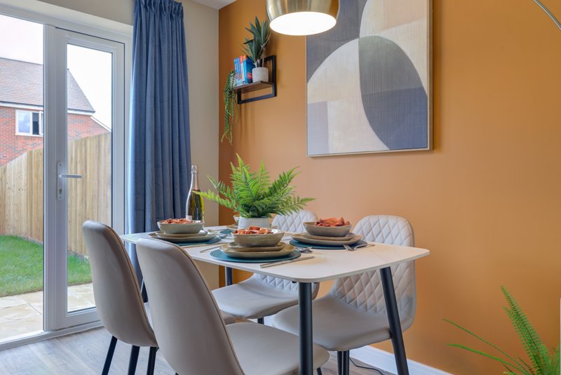 Dining area with table, grey chairs, orange walls, pendant lamp and garden view