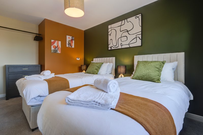 Modern bedroom with three single beds, green accent wall, orange feature wall, and contemporary artwork