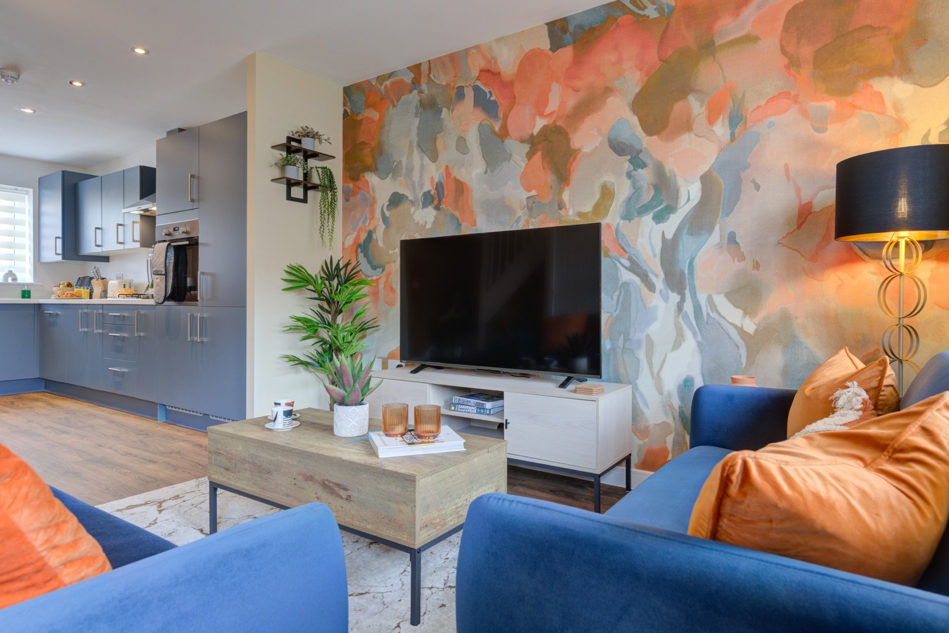 Modern open-plan living room with blue sofas, TV, abstract wall art and kitchen visible