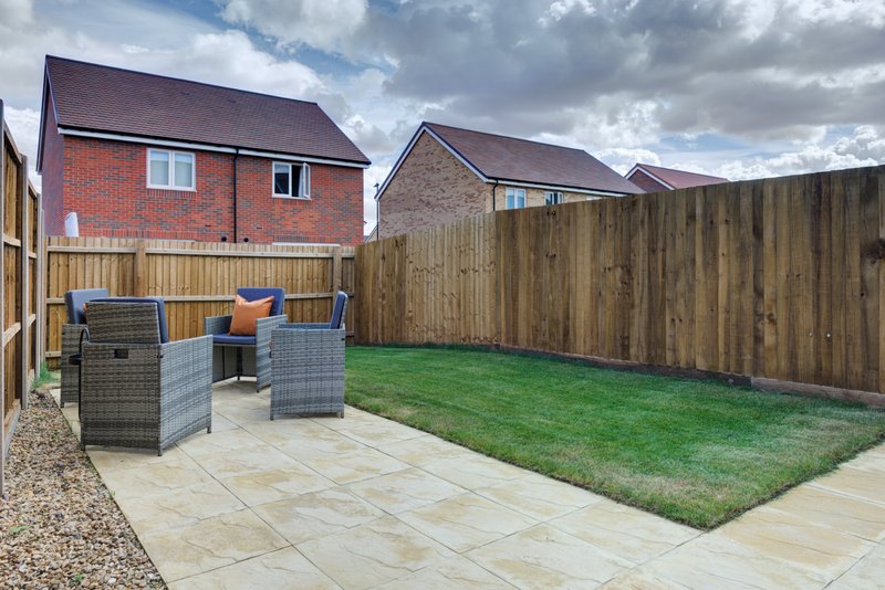 Rear garden with patio seating area, lawn, wooden fence and brick houses