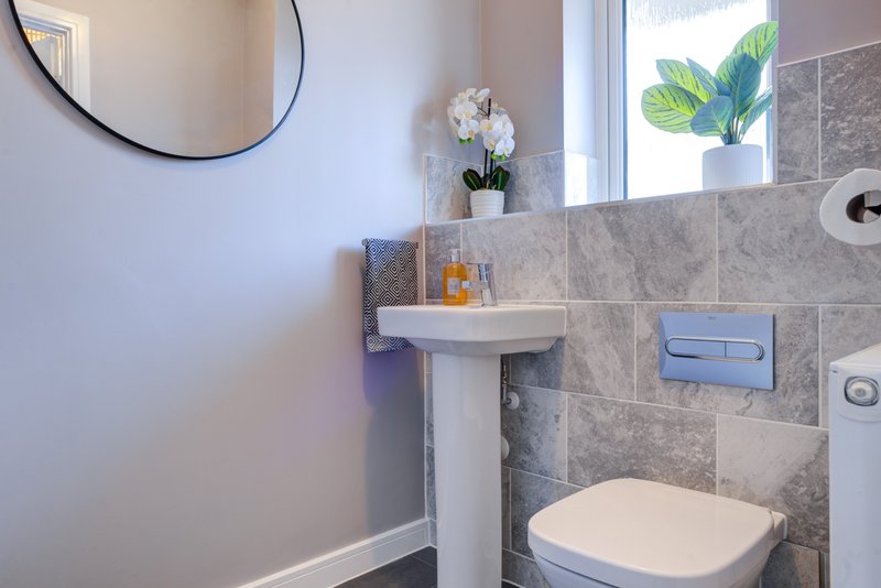 Modern bathroom with pedestal sink, gray tile walls, toilet, and round mirror