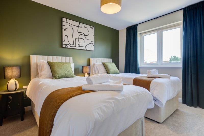 Modern bedroom with two twin beds, green walls, artwork and blue curtains