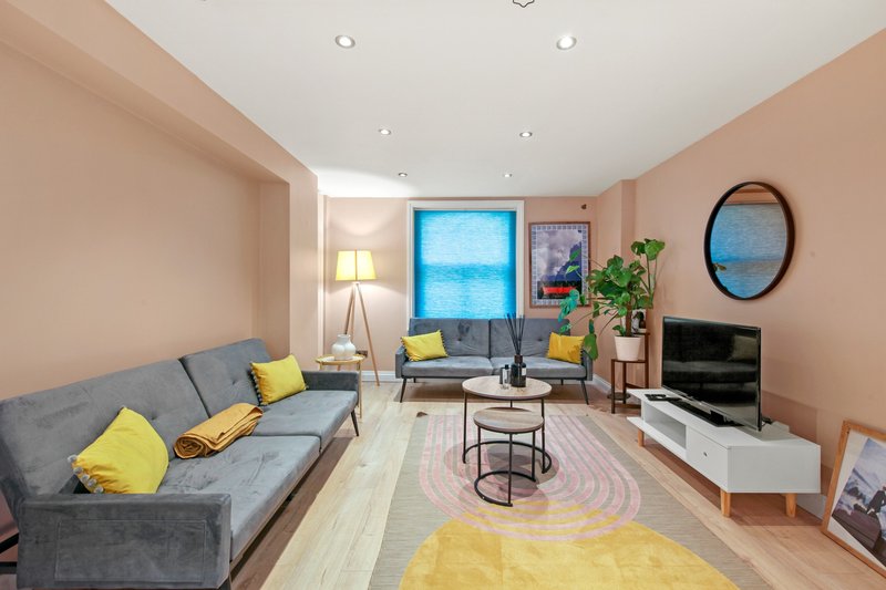 Modern living room with gray sofas, yellow cushions, blue window, TV and round mirror