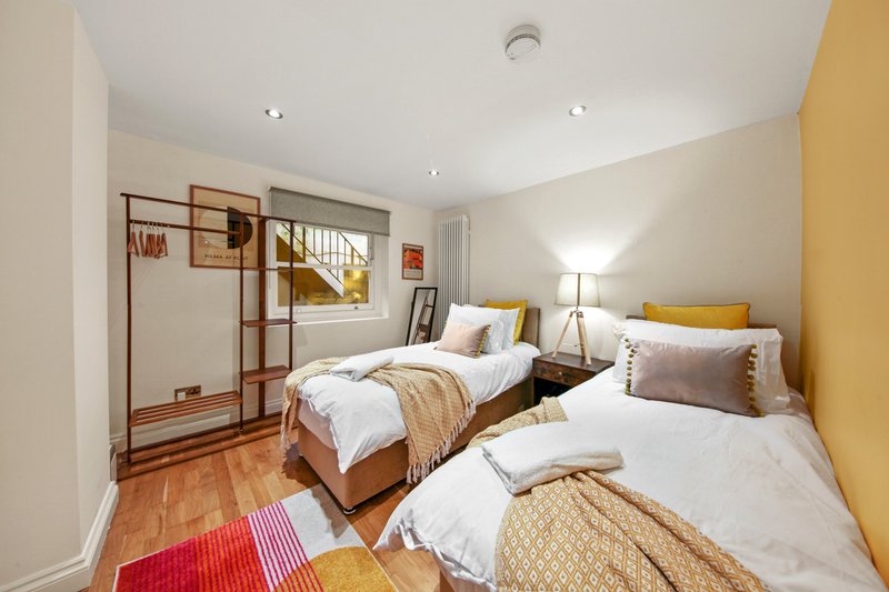 Bright bedroom with two single beds, wooden flooring, yellow accent wall and modern furnishings