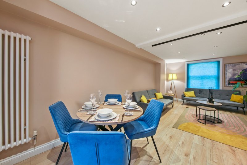 Open-plan dining and living area with blue chairs, round table, and yellow accents