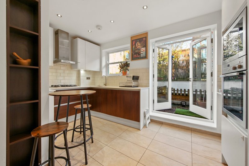Modern kitchen with white cabinetry, wood accents, bar seating, and patio doors opening to garden
