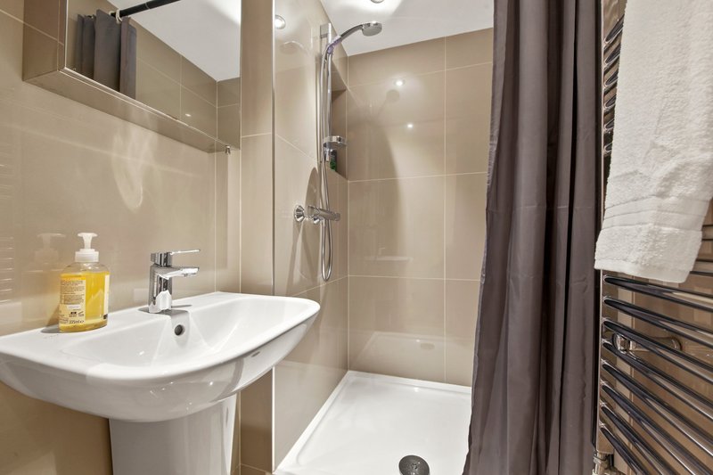 Modern bathroom with pedestal sink, shower enclosure, beige tiles and heated towel rail