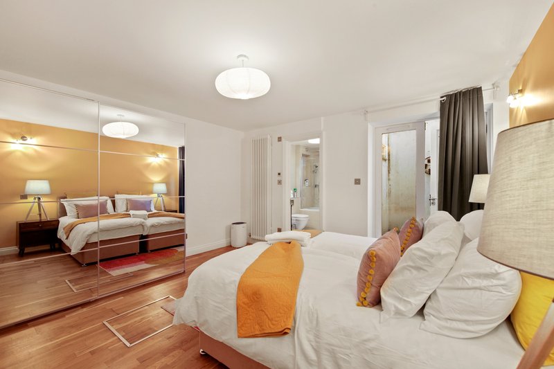 Modern bedroom with two beds, mirrored wardrobe, wooden flooring and en-suite bathroom access