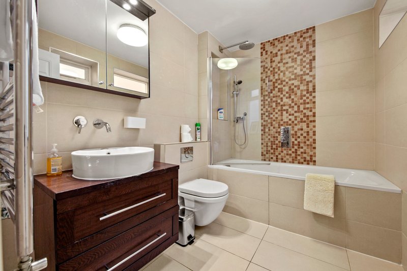 Modern bathroom with wooden vanity, round basin, toilet, bathtub and mosaic tile shower wall