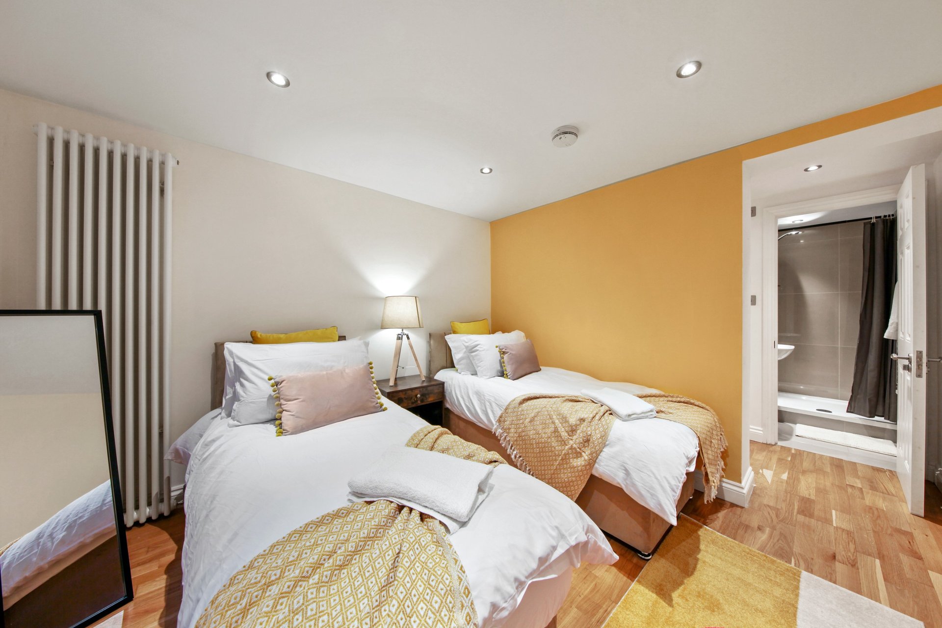 Bright bedroom with two single beds, yellow accent wall, wooden floor and ensuite bathroom