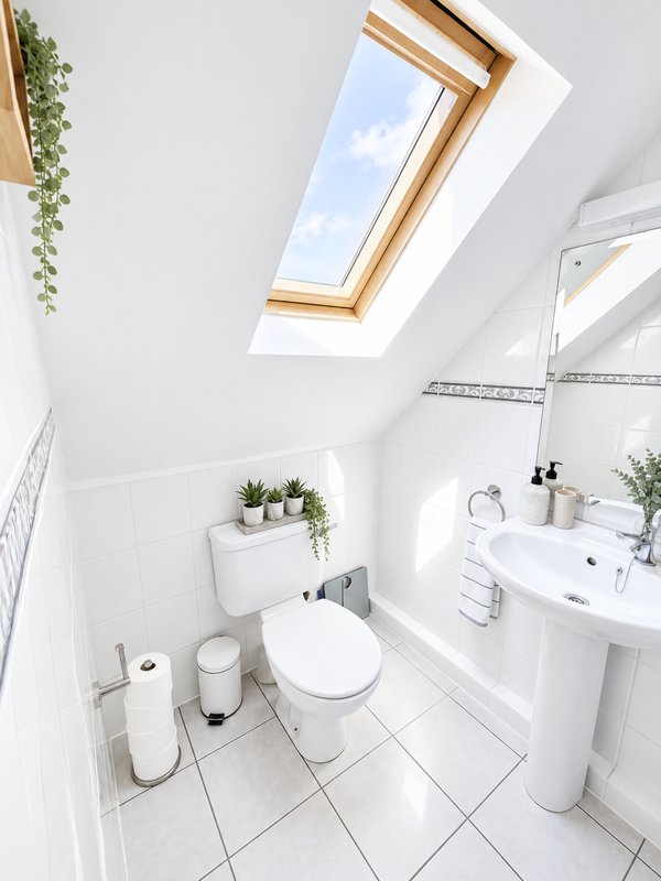 Bright modern bathroom en-suite with skylight, white tiles, pedestal sink, toilet and shower