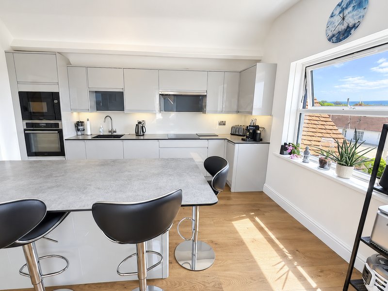 Modern white kitchen with breakfast bar seating four, and coastal sea view from large window