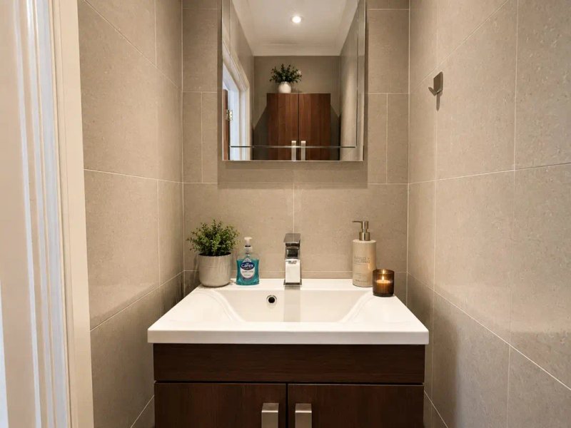 Modern bathroom with white sink, dark wooden vanity, mirror, and beige tile walls