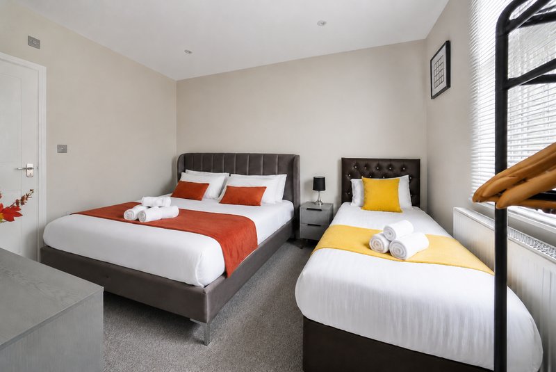 Twin bedroom with two single beds, orange and yellow bedding, dark headboards and carpeted floor