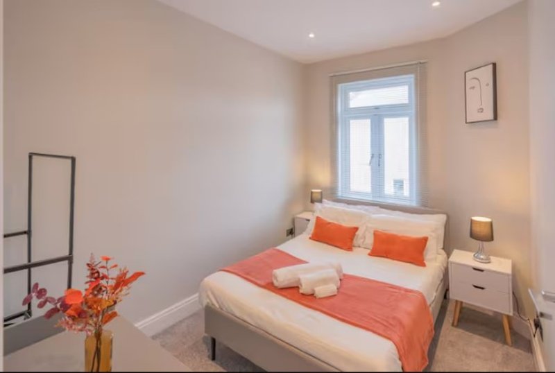 Bright modern bedroom with double bed, orange bedding, bedside tables and window